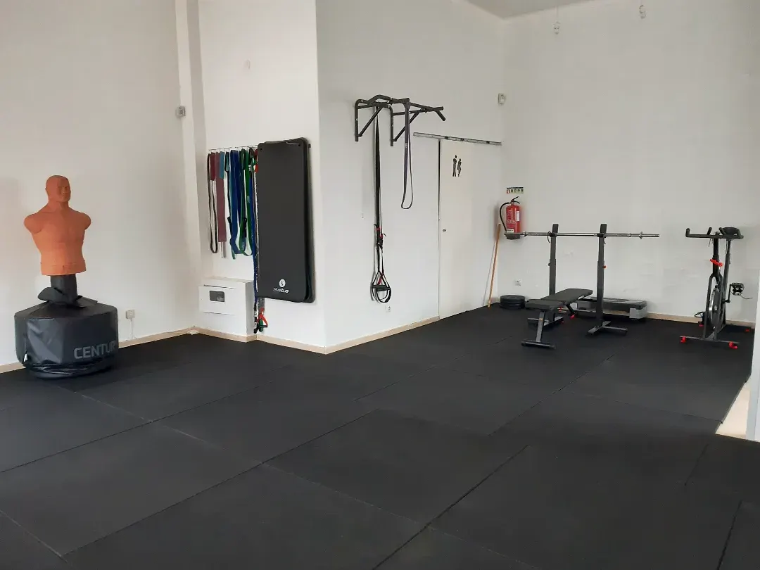 Sala de treino do estúdio com rack, saco de boxe e chão de borracha